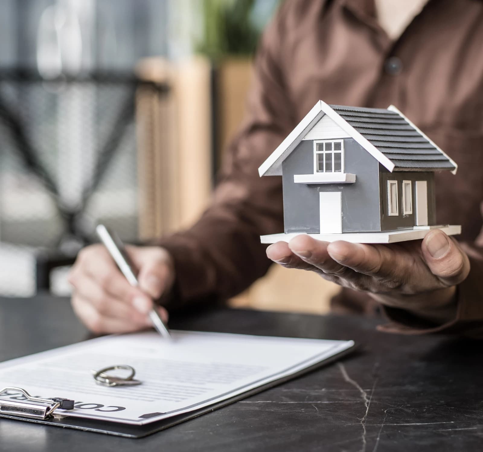 A model house held over a contract and pen on a desk